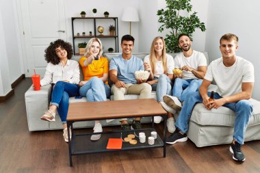 Mutlu bir şekilde gülümseyen bir grup genç arkadaş evde film izliyor..