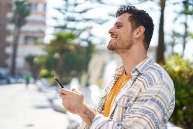 Parkta akıllı telefon kullanarak gülümseyen İspanyol genç adam.