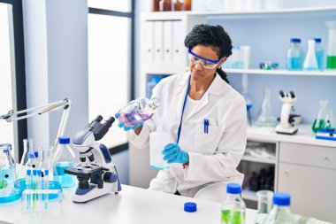 Laboratuvarda sıvı ölçen bilim adamı üniforması giyen Afrikalı Amerikalı kadın.
