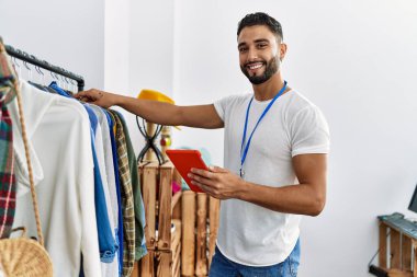 Genç Arap esnaf dokunmatik pedini kullanarak giyim mağazasında duruyor.