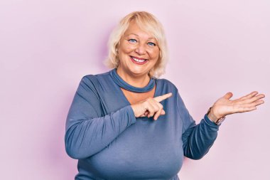 Orta yaşlı, sıradan kıyafetler giyen sarışın kadın kameraya hayret ediyor ve gülümsüyor.. 