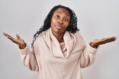 African woman standing over white background clueless and confused expression with arms and hands raised. doubt concept. 