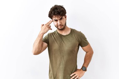 Hispanic man standing over isolated white background shooting and killing oneself pointing hand and fingers to head like gun, suicide gesture. 