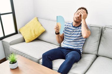 Genç İspanyol adam evde yelpaze kullanıyor.