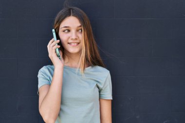 Sevimli bir kız gülümsüyor. Akıllı telefondan siyah arka planda konuşuyor.