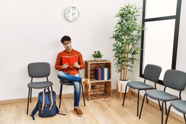 Young hispanic man reading book at waiting room