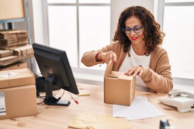 Middle age hispanic woman working packing a box at ecommerce