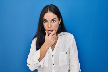 Mavi arka planda duran Latin kökenli genç kadın elleri çenesinde olan inanılmazlıktan, şaşkınlıktan ve şaşkınlıktan büyülenmiş görünüyor. 