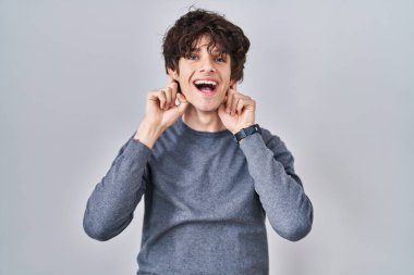 İzole edilmiş arka planda duran genç adam gülümsüyor parmaklarıyla kulaklarını çekiyor, komik bir jest. deneme sorunu 