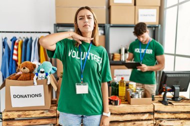 Young blonde girl wearing volunteer t shirt at donation stand cutting throat with hand as knife, threaten aggression with furious violence 