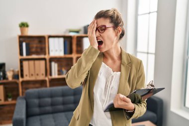 Young woman working at consultation office yawning tired covering half face, eye and mouth with hand. face hurts in pain. 