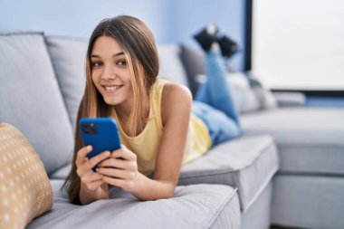 Evdeki kanepede uzanmış akıllı telefon kullanan sevimli kız.