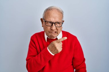 Senior man with grey hair standing over isolated background pointing aside worried and nervous with forefinger, concerned and surprised expression 