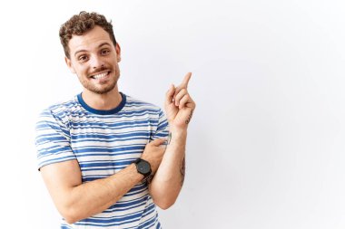 Yakışıklı genç adam izole edilmiş arka planda duruyor. Yüzünde kocaman bir gülümseme var. Parmağıyla kameraya bakıyor.. 