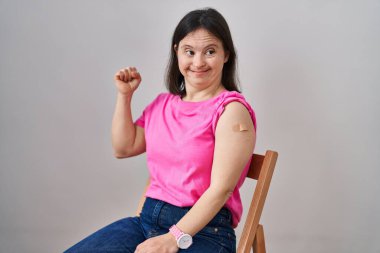 Woman with down syndrome wearing band aid for vaccine injection screaming proud, celebrating victory and success very excited with raised arms 