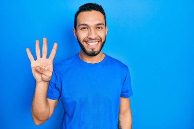 Hispanic man with beard wearing casual blue t shirt showing and pointing up with fingers number four while smiling confident and happy. 