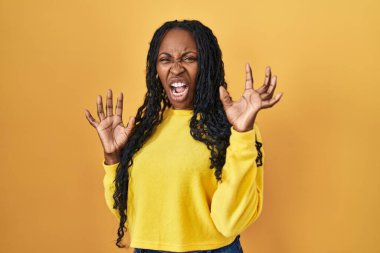 African woman standing over yellow background afraid and terrified with fear expression stop gesture with hands, shouting in shock. panic concept. 