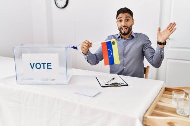 Siyasi seçim kampanyasında sakallı genç yakışıklı adam, elinde Venezuela bayrağı, zaferi mutlu bir gülümseme ve ellerini kaldırarak kazanan ifadeyle kutluyor. 