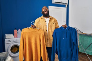 Afro-Amerikalı adam çamaşır odasında askı üzerinde temiz giysiler tutuyor kızgın ve kızgın çığlıklar atıyor sinirli ve öfkeli, öfkeyle bağırıyor.. 