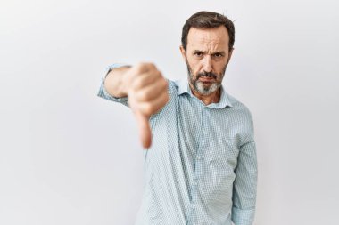 Middle age hispanic man with beard standing over isolated background looking unhappy and angry showing rejection and negative with thumbs down gesture. bad expression. 
