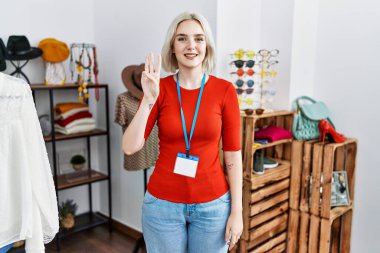 Young caucasian woman working as manager at retail boutique showing and pointing up with fingers number three while smiling confident and happy. 