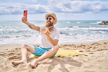 Genç kızıl saçlı adam kokteyl içiyor sahildeki akıllı telefonun yanında selfie çekiyor..