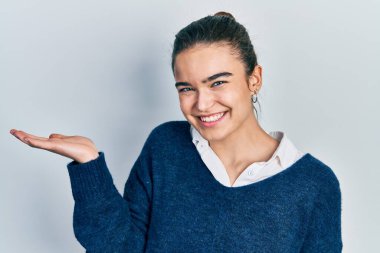 Gündelik giysiler giyen, neşeli gülümseyen, avuç içiyle kameraya bakan beyaz bir kız.. 