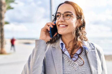 Genç İspanyol kadın yönetici deniz kenarında akıllı telefondan konuşuyor.