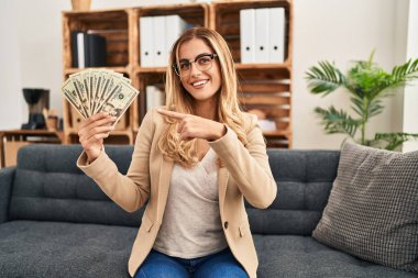 Terapi ofisinde çalışan genç sarışın kadın elinde para tutarken mutlu bir şekilde elini ve parmağını gösterdi. 