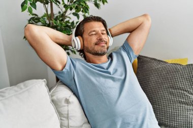 Middle age caucasian man relaxed with hands on head listening to music at home