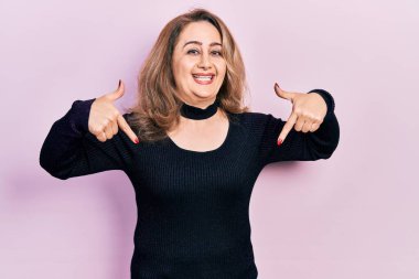 Orta yaşlı, günlük kıyafetler giyen, kendine güvenen, gülümseyen, kendini gururlu ve mutlu gösteren beyaz bir kadın.. 