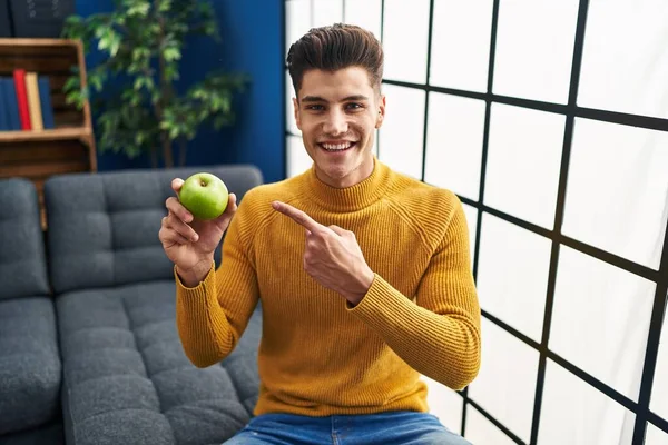 Young Hispanic Man Holding Green Apple Smiling Happy Pointing Hand — Zdjęcie stockowe