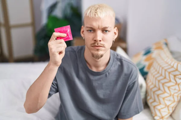 Young Caucasian Man Holding Condom Sitting Bed Thinking Attitude Sober — Stock Photo, Image
