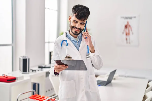 Young Hispanic Man Wearing Doctor Uniform Talking Smartphone Reading Medical — Stok fotoğraf