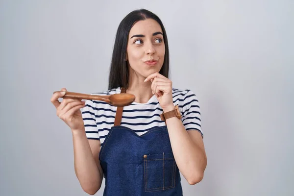 Young Brunette Woman Wearing Apron Tasting Food Holding Wooden Spoon — Zdjęcie stockowe