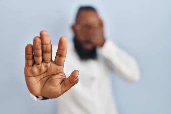 アフリカ系アメリカ人の男性が青い背景に手で目を覆い 悲しみと恐怖の表情でジェスチャーを止めます 恥をかかせ否定的な概念 — ストック写真