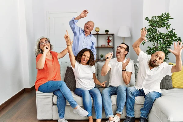 Group of middle age friends having party singing song using microphone at home.