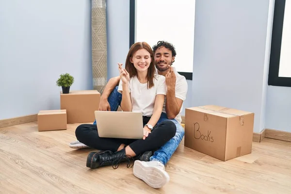 Young Couple Using Laptop New Home Gesturing Finger Crossed Smiling — Fotografia de Stock