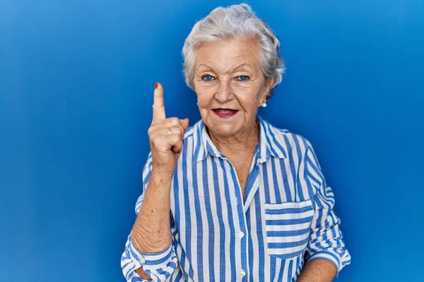 Старшая Женщина Седыми Волосами Стоит Синем Фоне Показывает Пальцем Номер — стоковое фото