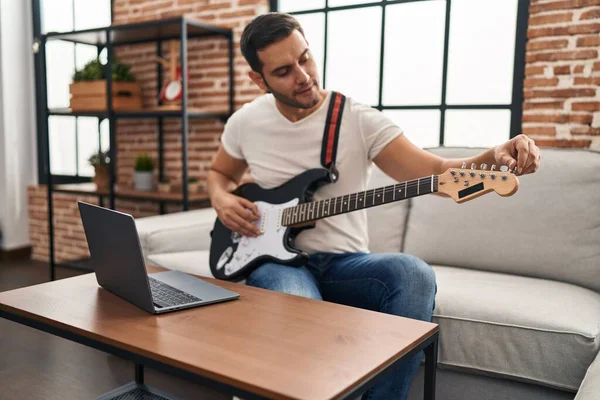 Young hispanic man having online electrical guitar class at home