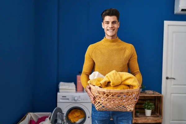 Young hispanic man holding laundry basket smiling with a happy and cool smile on face. showing teeth.