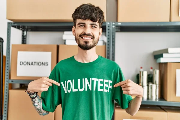 Young Hispanic Man Pointing Volunteer Uniform Working Charity Center — Stock Photo, Image