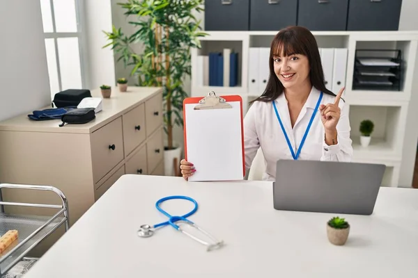 Junge Brünette Ärztin Mit Klemmbrett Lächelt Glücklich Und Zeigt Mit — Stockfoto