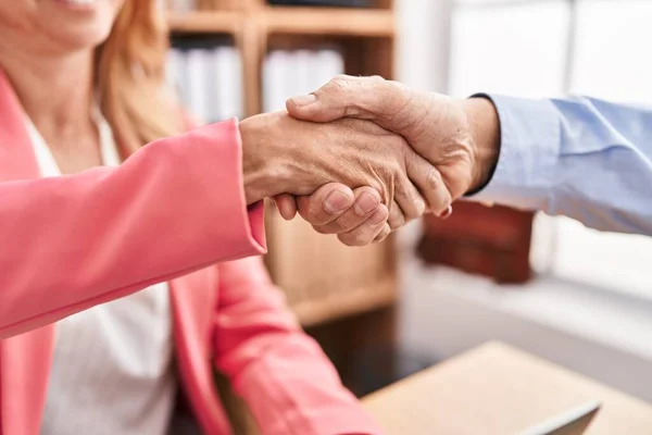 Middle age man and woman business workers shake hands at office