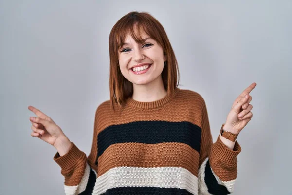 年轻美丽的女人穿着条纹毛衣 披着孤立的背景微笑着 用手指指向不同的方向 充满自信 复制广告空间 — 图库照片