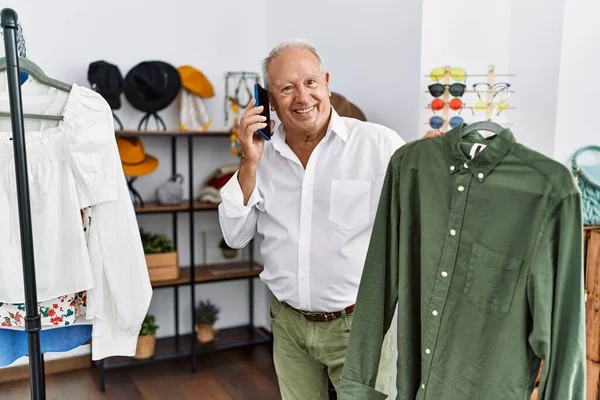 Senior man customer talking on the smartphone holding shirt at clothing store