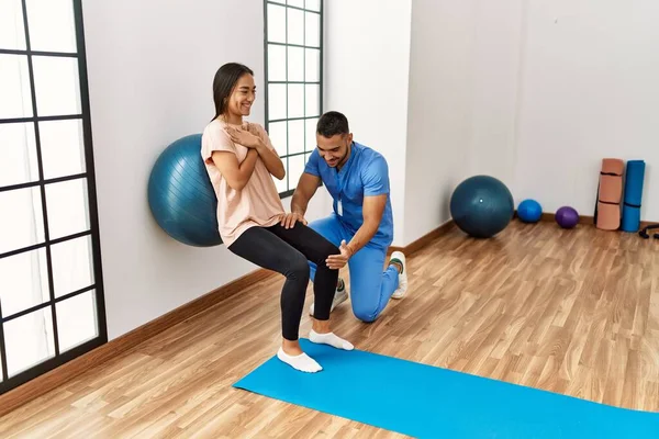 Latin man and woman wearing physiotherapist uniform having rehab session using fit ball at rehab center