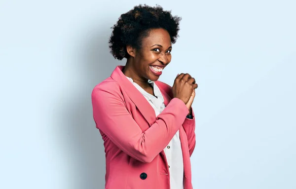 African american woman with afro hair wearing business jacket laughing nervous and excited with hands on chin looking to the side