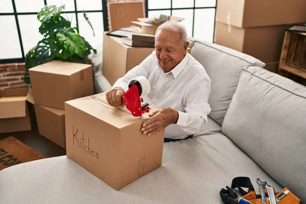 Senior man smiling confident packing cardobard box at new home
