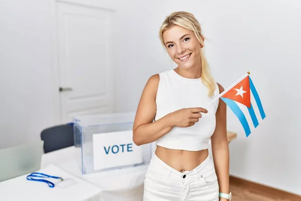 Young caucasian woman at political campaign election holding cuba flag looking positive and happy standing and smiling with a confident smile showing teeth